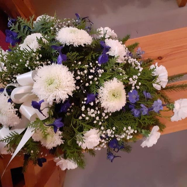 Violeteista ja valkoisista kukista sidottu hautajaiskimppu